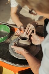 Potter creating vase with clay on pottery wheel with apprentice