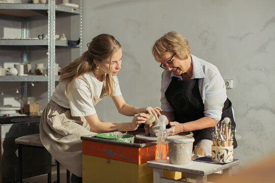 Senior woman learning pottery with young instructor in workshop