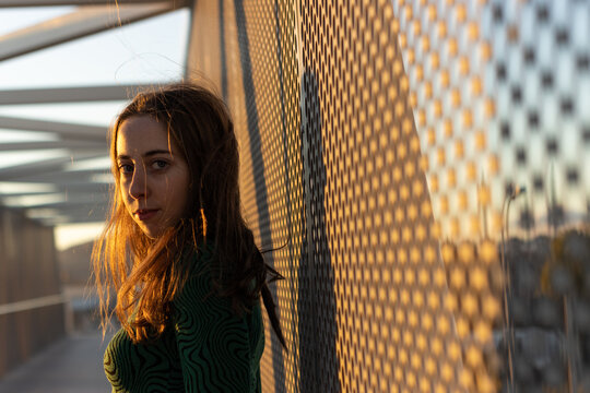 Young woman leaning against a metal fence on a bridge at sunset
