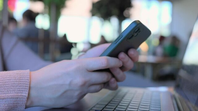 A person uses a smartphone while working on a laptop in a vibrant caf setting