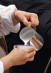 Close-up of a barista pouring freshly steamed milk into the porcelain cup, preparing a hot beverage with care and precision. Ideal image showcasing coffee preparation or barista skills.