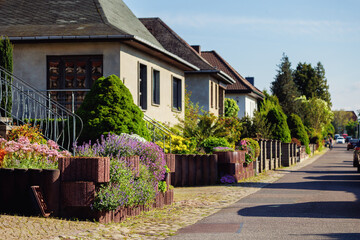 City street of single-family modern houses Germany blooming flowers bed  green bush hedge. German suburban small town residential area row eco sustainable life building neighborhood suburb