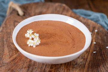 Smooth chocolate mousse in a white bowl, garnished with delicate white flowers, presented on a...