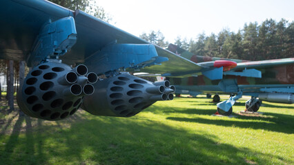 A vintage Soviet aircraft rests in a green park with missile pods prominently featured under the...