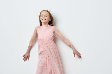 Cheerful girl in a pink dress with flowing hair against a white background, smiling joyfully and...