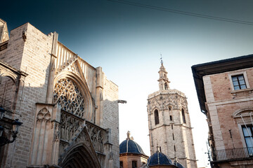 Gothic facade of Valencia Cathedral with ornate rose window rises beside the octagonal Micalet bell tower under evening sky, highlighting historic architecture that shapes the city’s old town skyline.