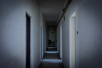 Dim abandoned hotel corridor strewn with debris and missing fixtures; doorframes recede into...