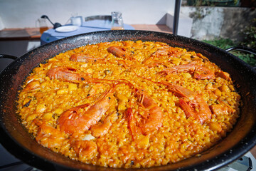Close-up view of traditional Valencian seafood paella (paella de mariscos) in black pan; saffron rice dotted with mussels and topped with whole prawns during an outdoor Mediterranean meal.
