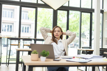 A woman is working at a desk in an office with a laptop, a mobile phone and a pile of documents. She is smiling and happy.
