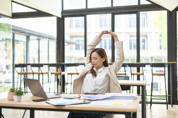 Fototapeta premium A woman is working at a desk in an office with a laptop, a mobile phone and a pile of documents. She is smiling and happy. 