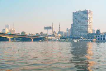 Obraz premium View of Cairo skyline with mosques, buildings, and a bridge reflected in the Nile River during the golden hour