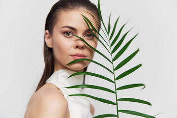 Naklejka premium Modern portrait of a woman with long hair holding a green palm leaf, showcasing natural beauty and elegance in a minimalistic setting.