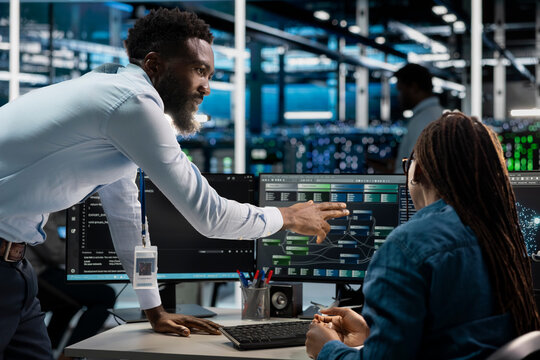 Data center computer scientists setting up machine learning node trees systems handling information. African american workers training neural networks to improve server farm operations
