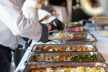 Catering staff serves a delicious buffet at a formal event in a well-lit hall during the afternoon
