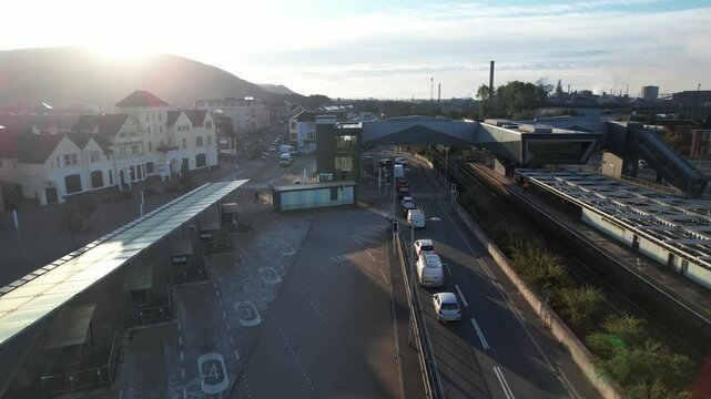 Public transport terminal in town. Forwards fly above road leading between train station and bus stops. View against low sun. Port Talbot, Wales, UK