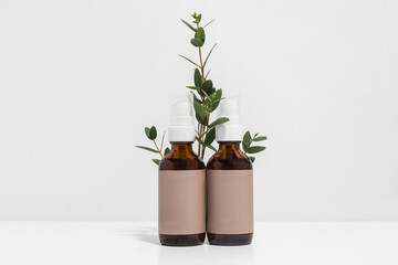 Two glass jars of face oil on white background with fresh eucalyptus 