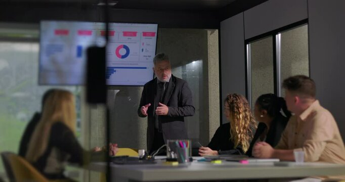 Corporate manager explaining report data to attentive colleagues in boardroom with screen displaying colorful charts and graphs - Powered by Adobe