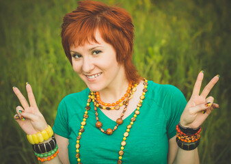 Happy young woman shows victory hand. Red-haired hippie girl in nature. Symbol of pacifism. International Day of Peace
