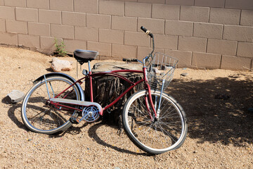 Abandoned kids bicycle with front wire basket leaned on huge tree stump next to block fence

