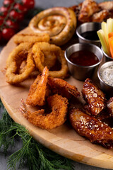 A beautifully arranged platter features a variety of gastronomic delights including crispy shrimp, savory onion rings, and flavorful chicken wings. Vegetables and sauces accentuate this feast