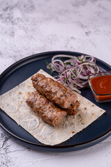 Grilled meat skewers rest upon a soft, flatbread, accompanied by a fresh onion salad and a vibrant, spicy sauce. A rustic culinary delight awaits the palate