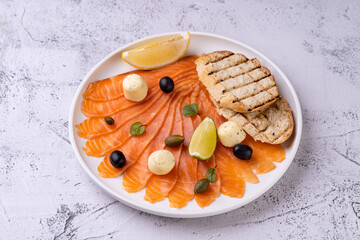 A beautifully arranged plate showcases thinly sliced salmon adjacent to toasted bread slices,...