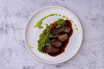 A beautifully presented dish features succulent, tender meat paired with vibrant green porridge and rich sauce, showcasing culinary expertise and aesthetic flair in fine dining