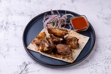 Juicy grilled meat pieces rest atop a piece of flatbread, garnished with fresh onions and a side of spicy sauce, creating an inviting plate of gastronomic pleasure
