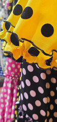 Brightly colored polka dot fabrics hang in layers, featuring bold yellow, black, pink, and white...