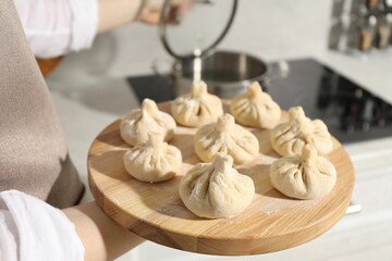 Woman with many uncooked khinkali near cooktop in kitchen, closeup