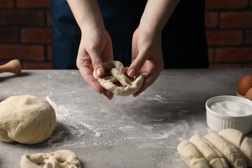 Woman making pretzel at light grey table, closeup