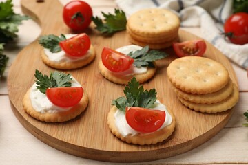 Tasty crackers with cream cheese, tomatoes and parsley on white wooden table, closeup