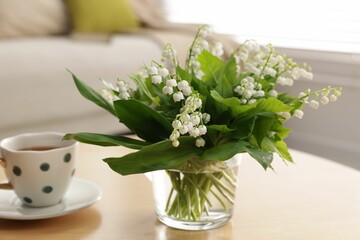 Bouquet of beautiful lily-of-the-valley and cup on table indoors, closeup