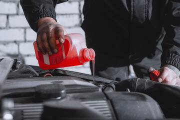 Close-up of a mechanic's dirty hands pouring red fluid into a car engine. Concept on car maintenance in garage conditions and engine care.