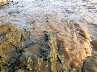 murky brown river water flows through natural rocks