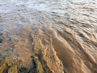 murky brown river water flows through natural rocks