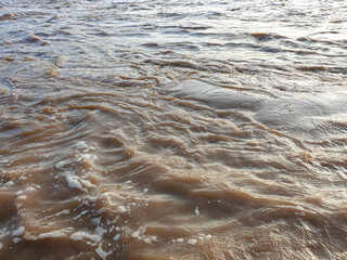 Brown Murky River Water Flowing Rapidly With Surface Ripples and Foam