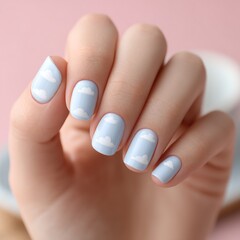 Light blue nails with white cloud designs are shown on a woman's hand, creating a soft, whimsical manicure look.