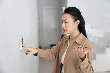 Woman standing indoors with concerned and frustrated expression while points at wall-mounted...