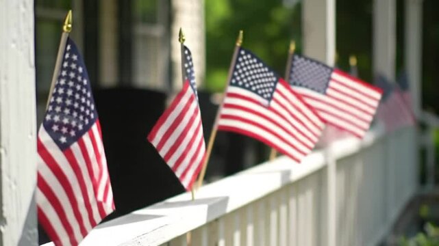 Multiple American flags waving on a white fence outdoors