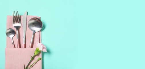 Napkin, cutlery and flower on turquoise background with space for text, closeup