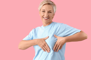 Beautiful mature woman checking her breast on pink background. Cancer awareness concept