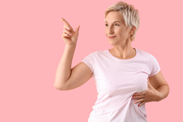 Beautiful mature woman pointing at something on pink background. Breast cancer awareness concept