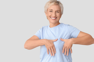 Smiling mature woman checking her breast on light background. Cancer awareness concept