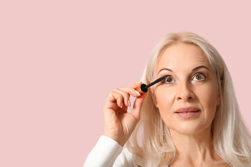 Beautiful mature woman applying mascara on pink background, closeup