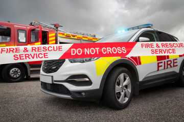 Emergency services fire brigade line - a cordoned off area with firefighting vehicle near fire engine. Department red fire truck appliance and equipment from fire station is in scene background. © Lawrey