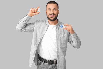 Young man holding eye drops and contact lenses on grey background