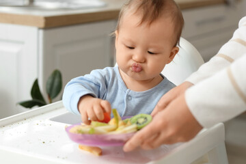 Mother feeding her little baby in high chair at home