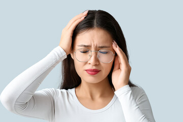 Young Asian woman suffering from headache on grey background. Brain Injury Awareness Month