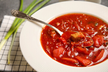 Bowl of tasty Ukrainian borscht and green onion on dark background, closeup